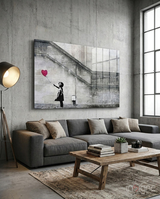 Flying Heart Glass Art displayed above a gray sectional sofa in an industrial loft showing a silhouetted girl reaching for a red heart balloon with "There is always hope" text.