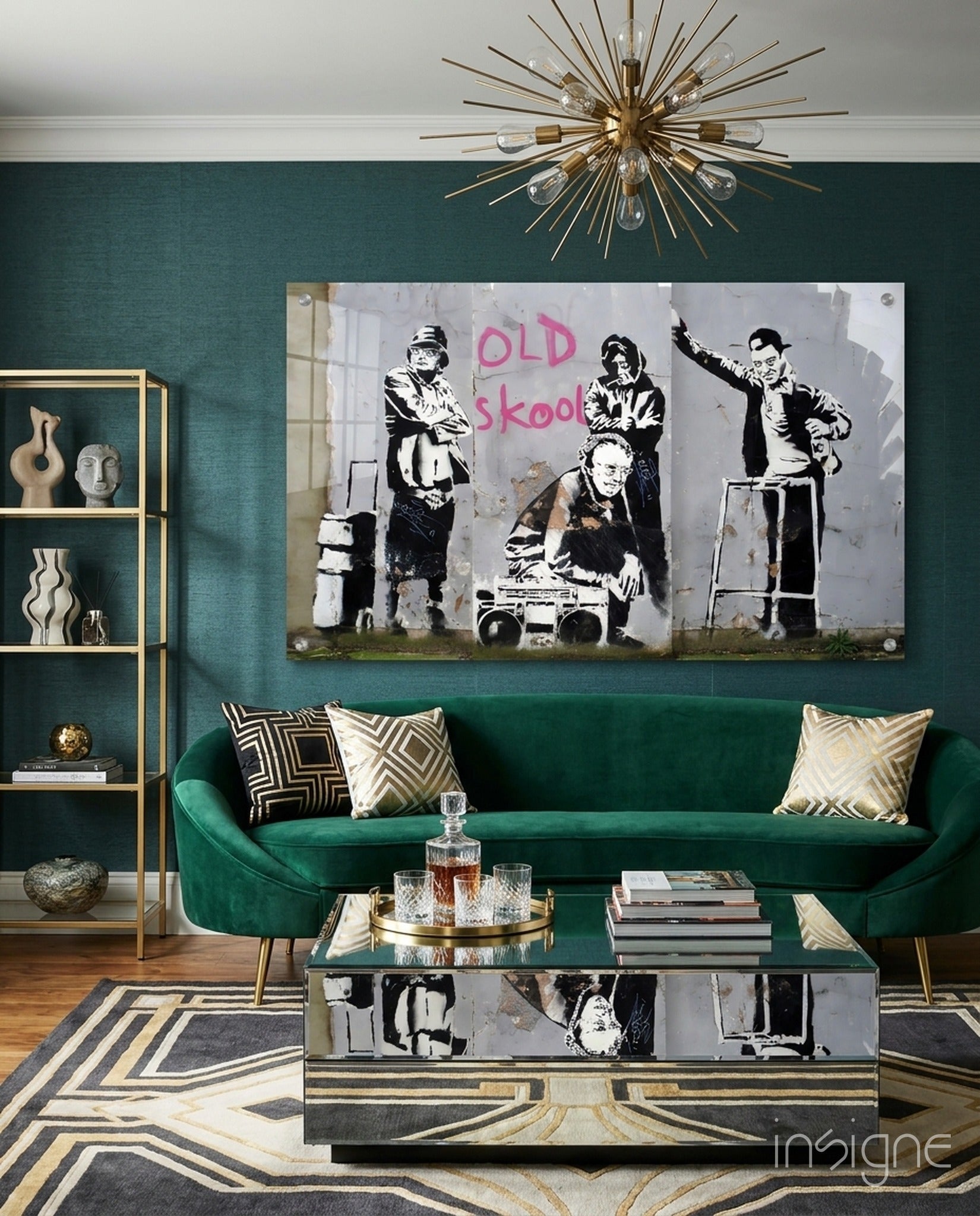 Banksy "Old Skool" street art print displayed above green velvet sofa in modern living room with gold accents.