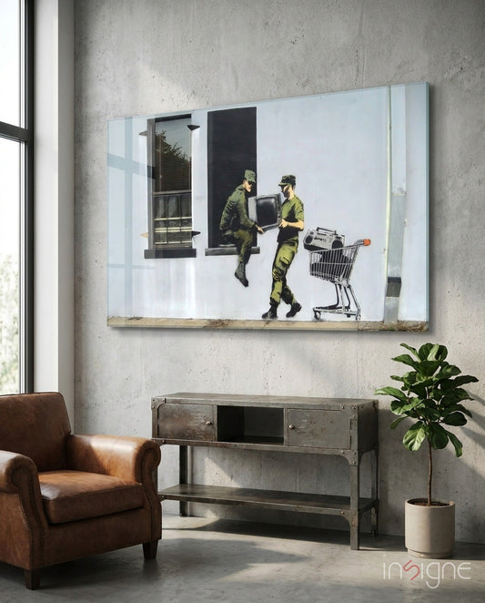 Glass art depicting two soldiers in camouflage uniforms exchanging a television and shopping cart displayed on concrete wall above industrial console table.