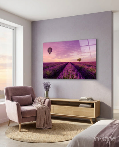 Glass art print of purple lavender field with hot air balloon and tree at sunset, displayed on bedroom wall above wooden console table.