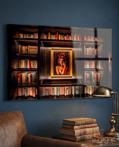 Glass art print of wooden bookshelf with gold-framed portrait, displayed on blue wall above leather chair and brass lamp.