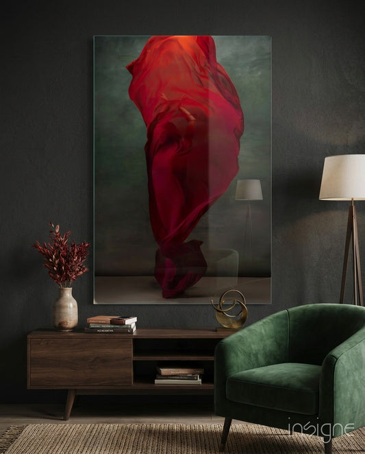 Framed glass wall art displaying a red silk fabric draped over an abstract form against a muted green-gray background, hung in a modern living room above a wooden console table.