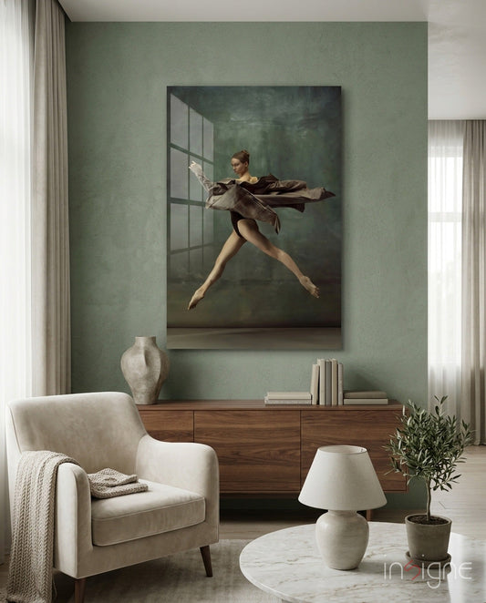 Framed glass wall art depicting a leaping ballerina in brown drape displayed above a wooden dresser in a sage green room.