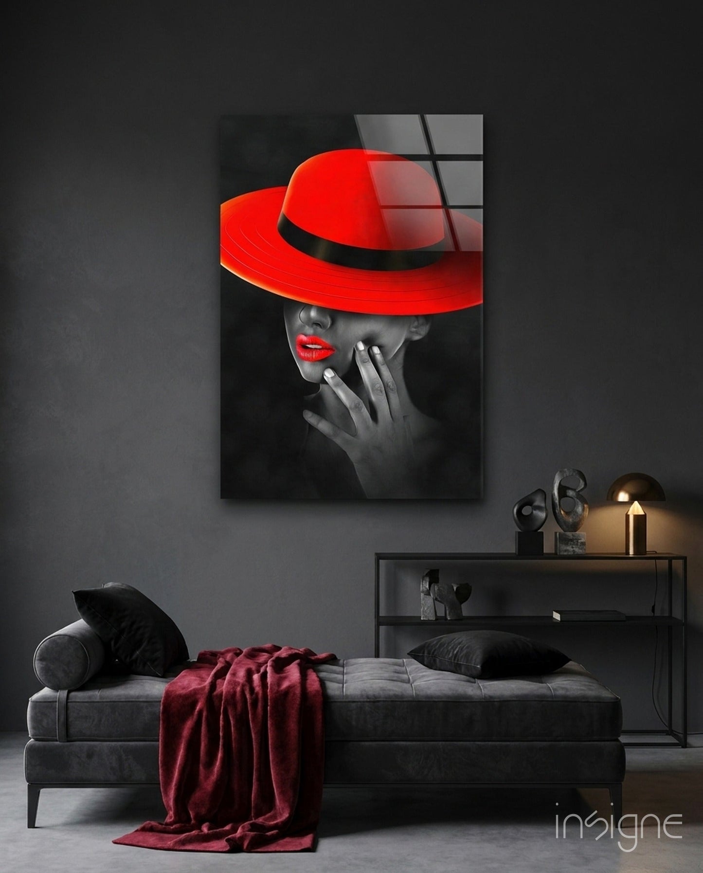 Scarlet Hat Glass Wall Art displayed above a gray sofa in a modern bedroom setting, showing a stylized portrait with vibrant red accents.