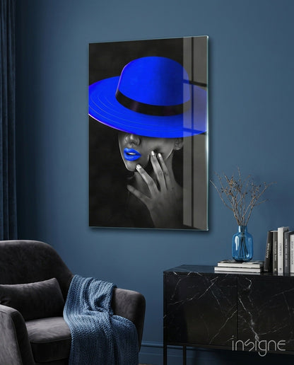 Blue Hat Glass Wall Art displayed on blue bedroom wall above black marble nightstand with books and vase.