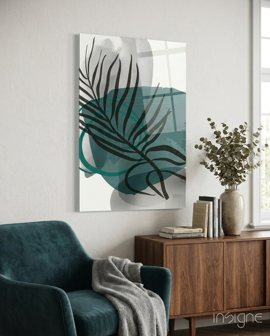 Abstract teal and black botanical glass art hanging above a teal chair and wooden cabinet with books and dried flowers.