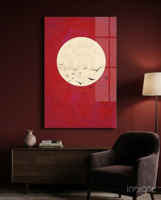Red glass wall art featuring a cream moon with black flying birds, displayed above a dark wooden dresser in a burgundy room.