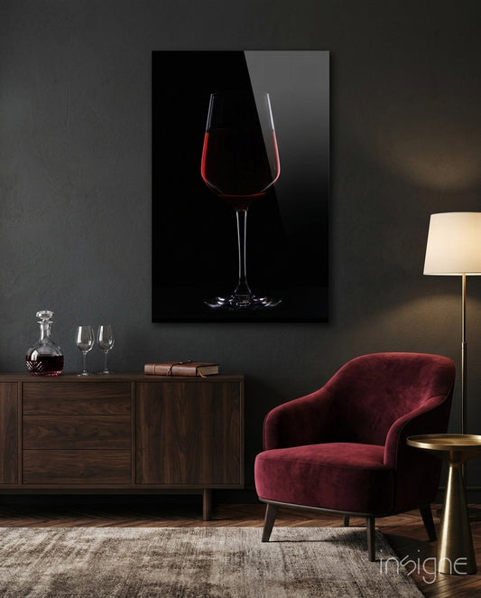 Half-filled red wine glass with glowing red liquid displayed on black glass mounted above wooden dresser in modern interior.