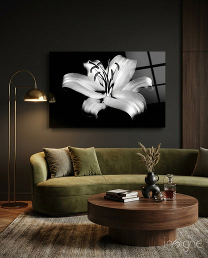Black and white lily glass wall art displayed above a curved green velvet sofa in a modern living room setting.