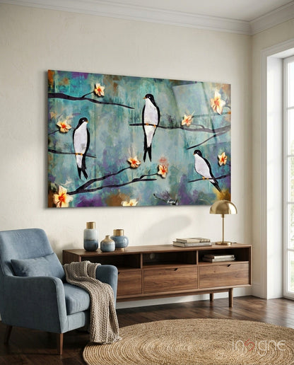 Glass wall art depicting black and white birds perched on branches with yellow flowers against a turquoise, purple, and gold textured background, displayed above a wooden console table in a living room.