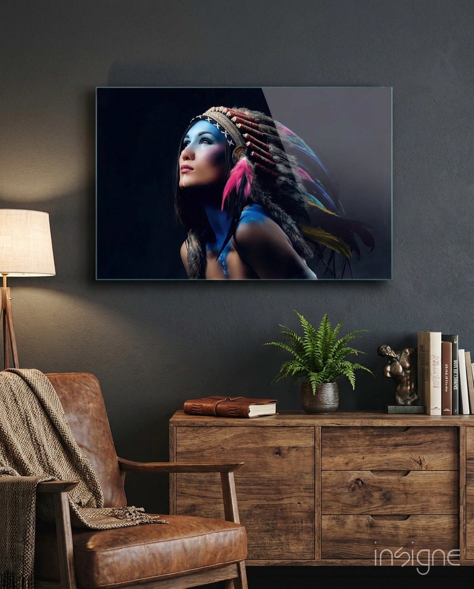 Glass wall art depicting a woman with blue face paint and colorful feathered headdress displayed in modern living room above wooden dresser.