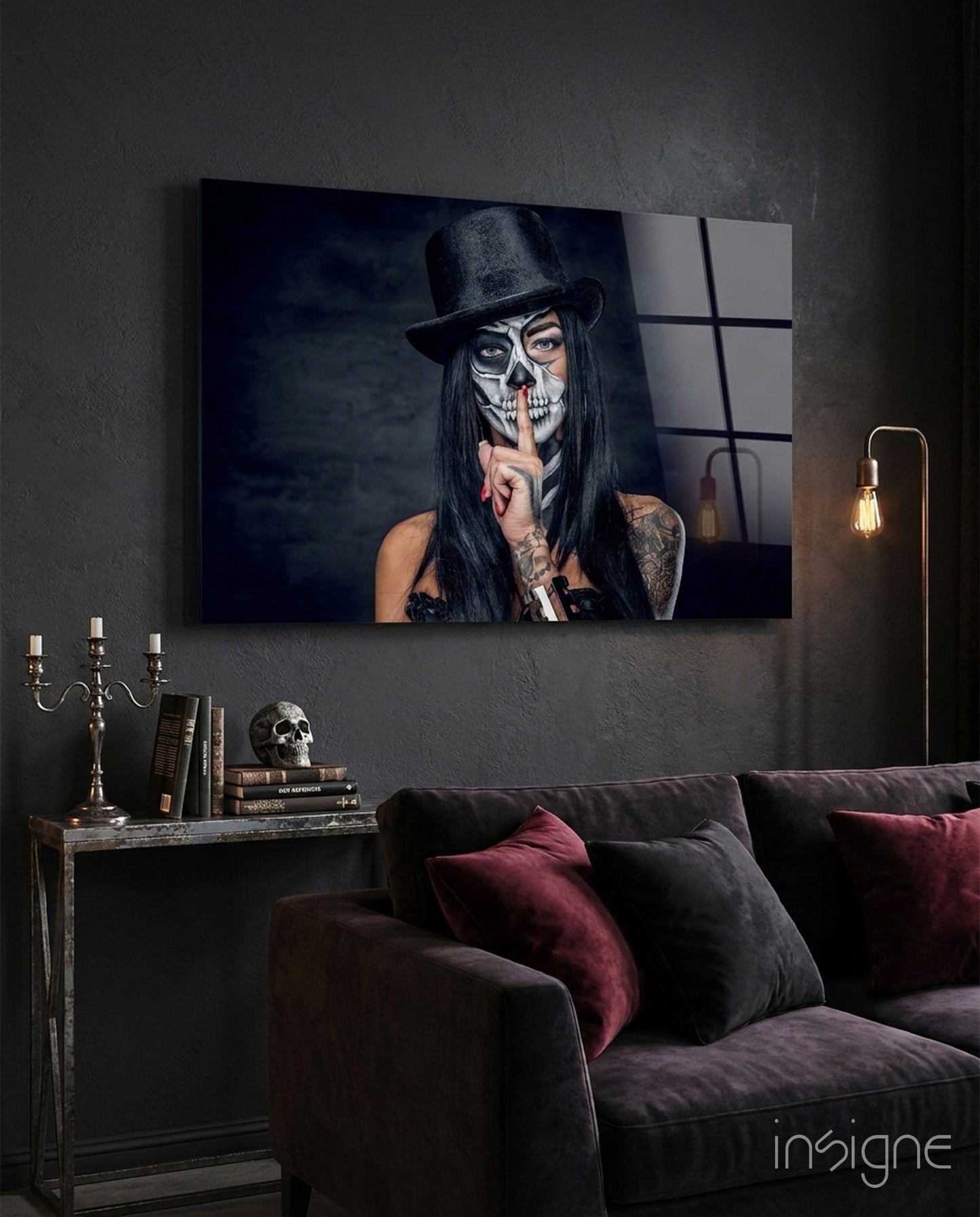 Glass wall art displaying skull-faced woman in black hat against dark interior with sofa and side table.