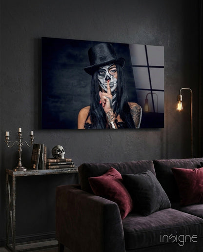 Glass wall art displaying skull-faced woman in black hat against dark interior with sofa and side table.