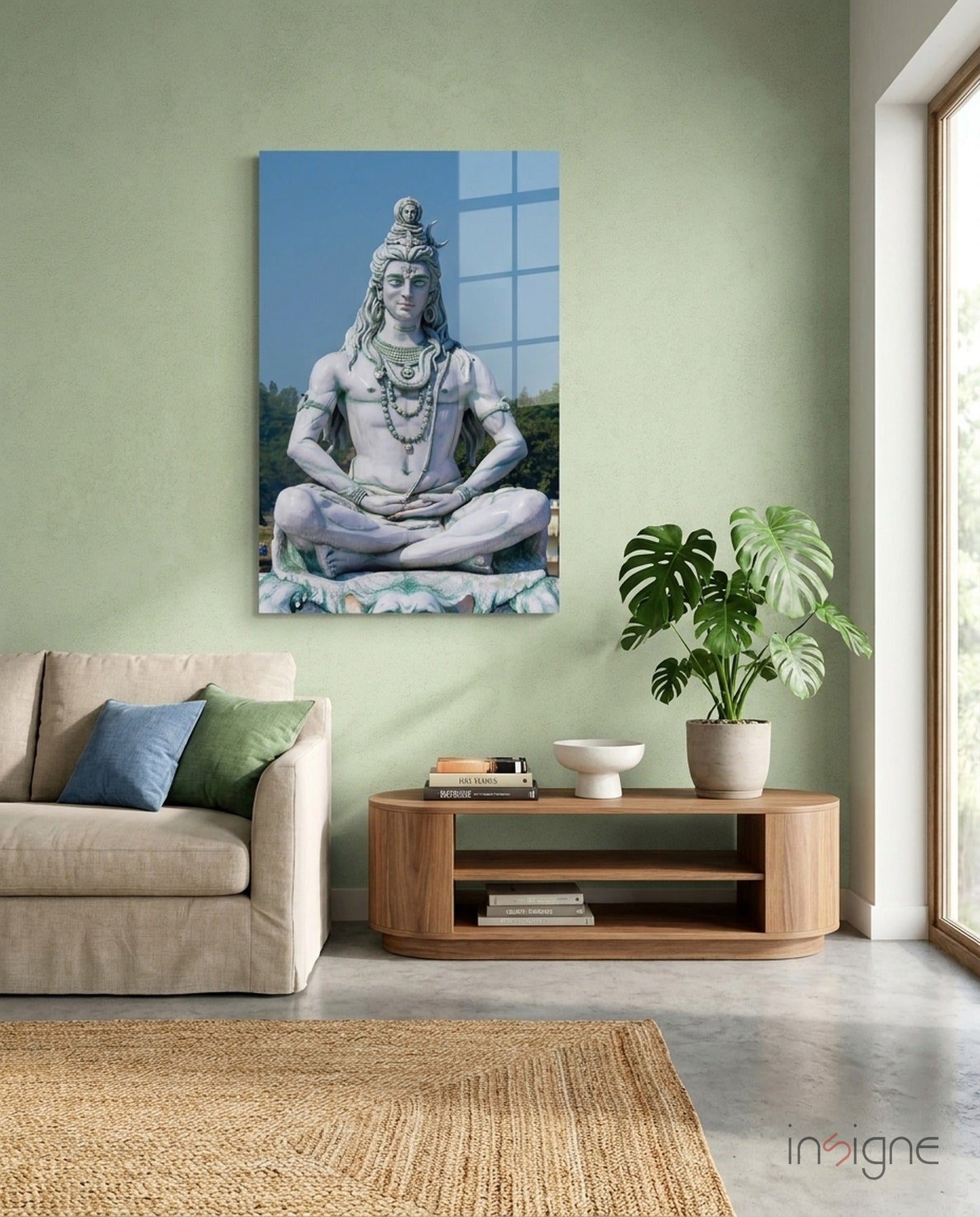 Glass wall art depicting Shiva in meditation pose displayed above wooden console table in sage green living room interior.
