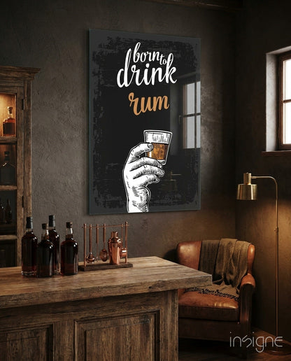 Neon-style wall art displaying "born to drink rum" in white and gold text with an illustrated hand holding a glass, mounted in a rustic bar setting above a wooden counter.