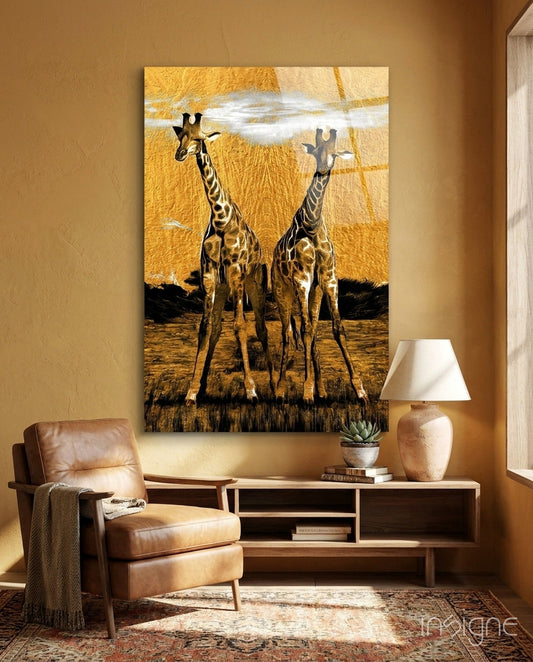 Glass wall art depicting two giraffes against golden sky displayed above wooden console in warm-toned room with leather chair.