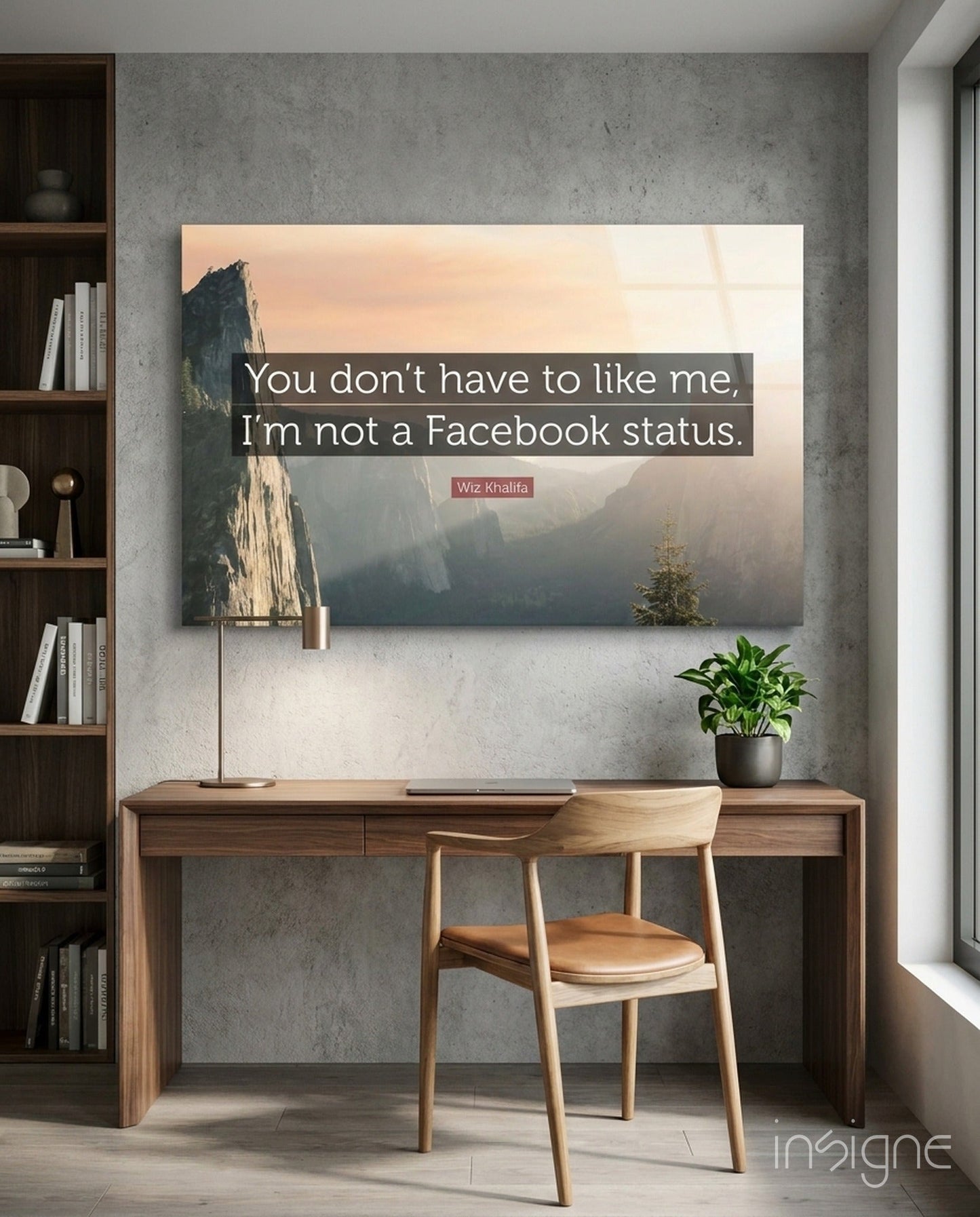 Glass wall art displaying a misty mountain landscape with text reading "You don't have to like me, I'm not a Facebook status" by Wiz Khalifa, mounted above a wooden desk.