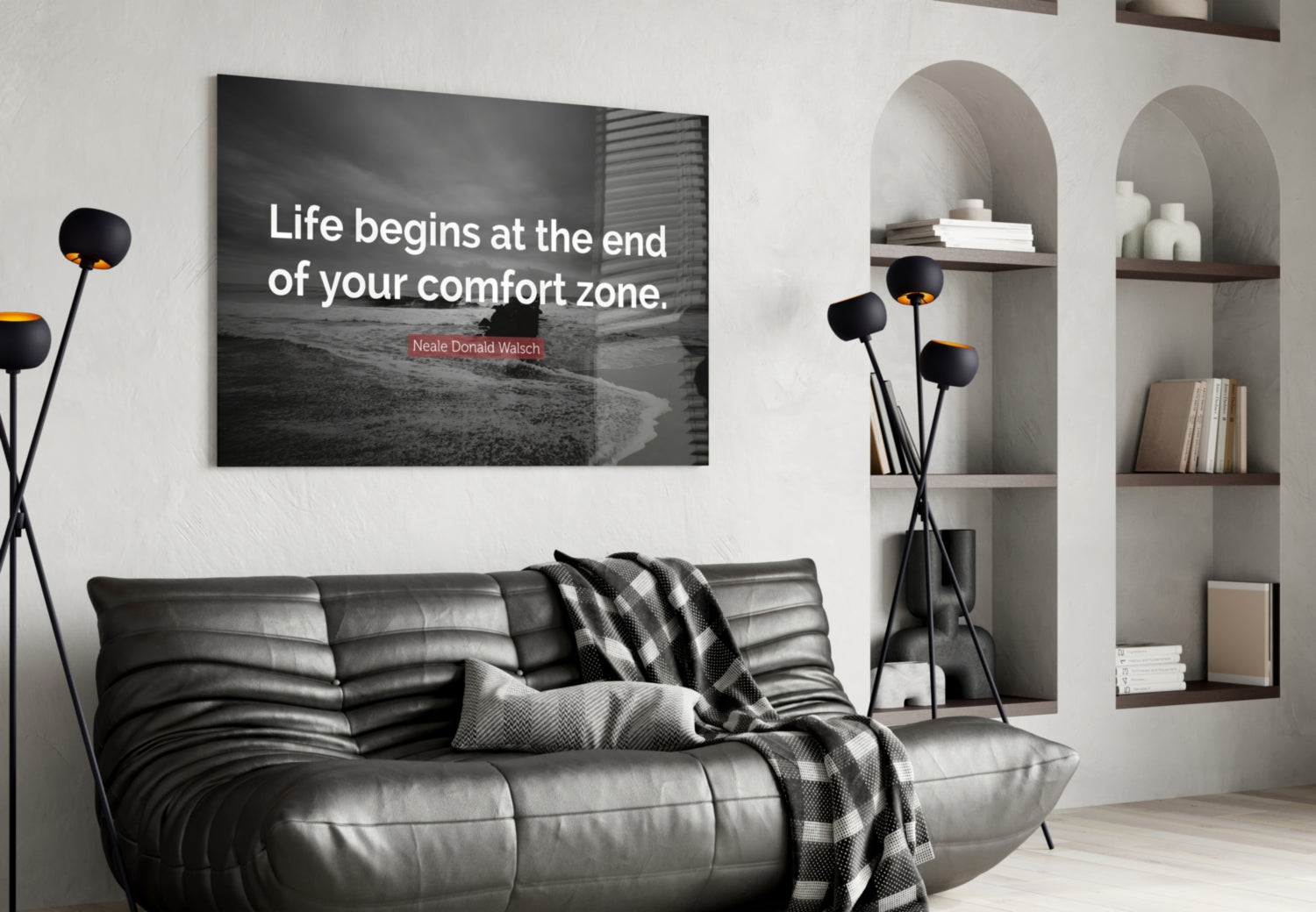 Modern living room interior with black leather sofa displaying glass wall art featuring quote "Life begins at the end of your comfort zone" above it.