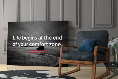 Black glass wall art with white text reading "Life begins at the end of your comfort zone" and attribution to Neale Donald Walsch, displayed in modern living room setting.