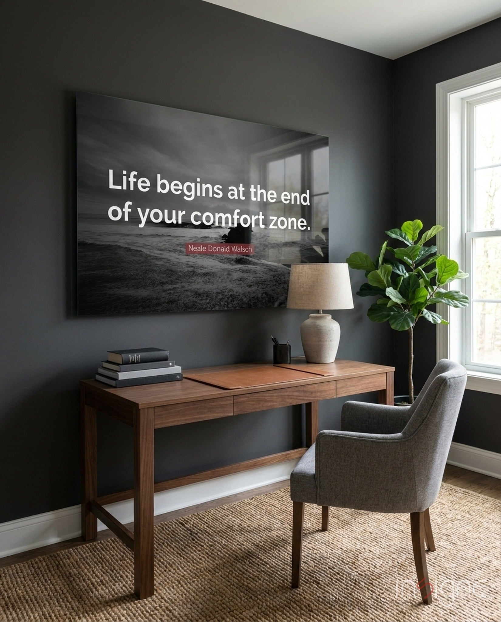 Black and white motivational glass wall art displaying "Life begins at the end of your comfort zone" quote above wooden desk in dark office.