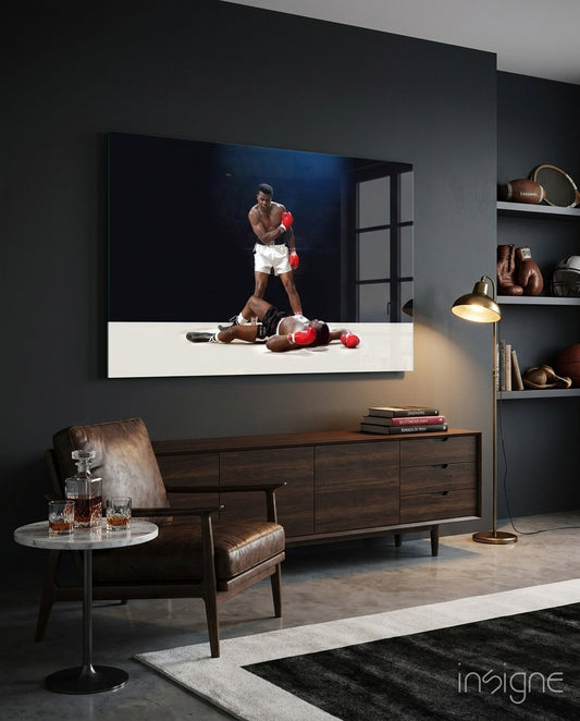 Glass wall art depicting a boxer standing over a fallen opponent, displayed in a modern living room with dark walls and mid-century furniture.