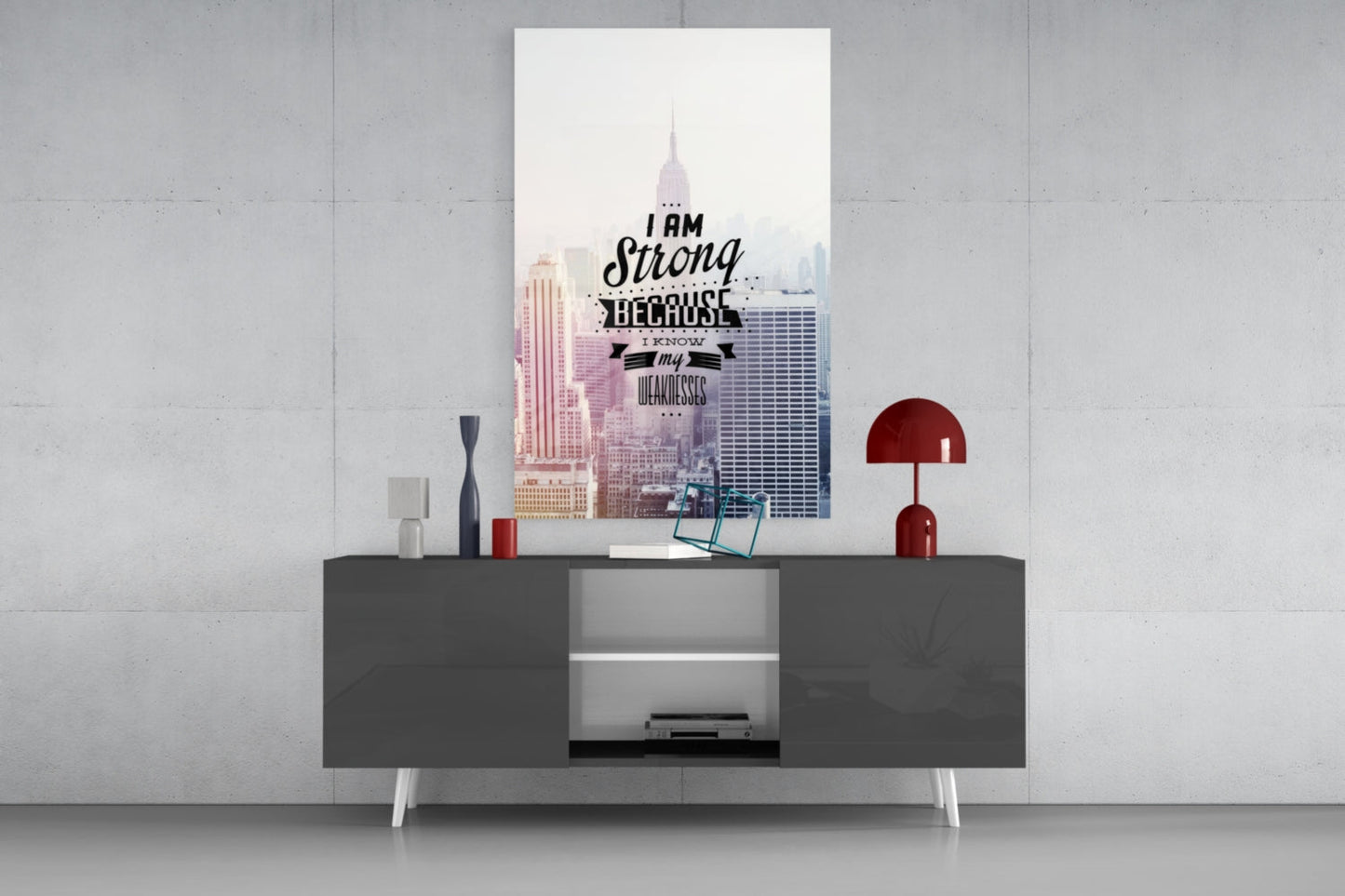 Modern living room setting displaying motivational glass wall art above gray media console with red lamp and decorative accessories.