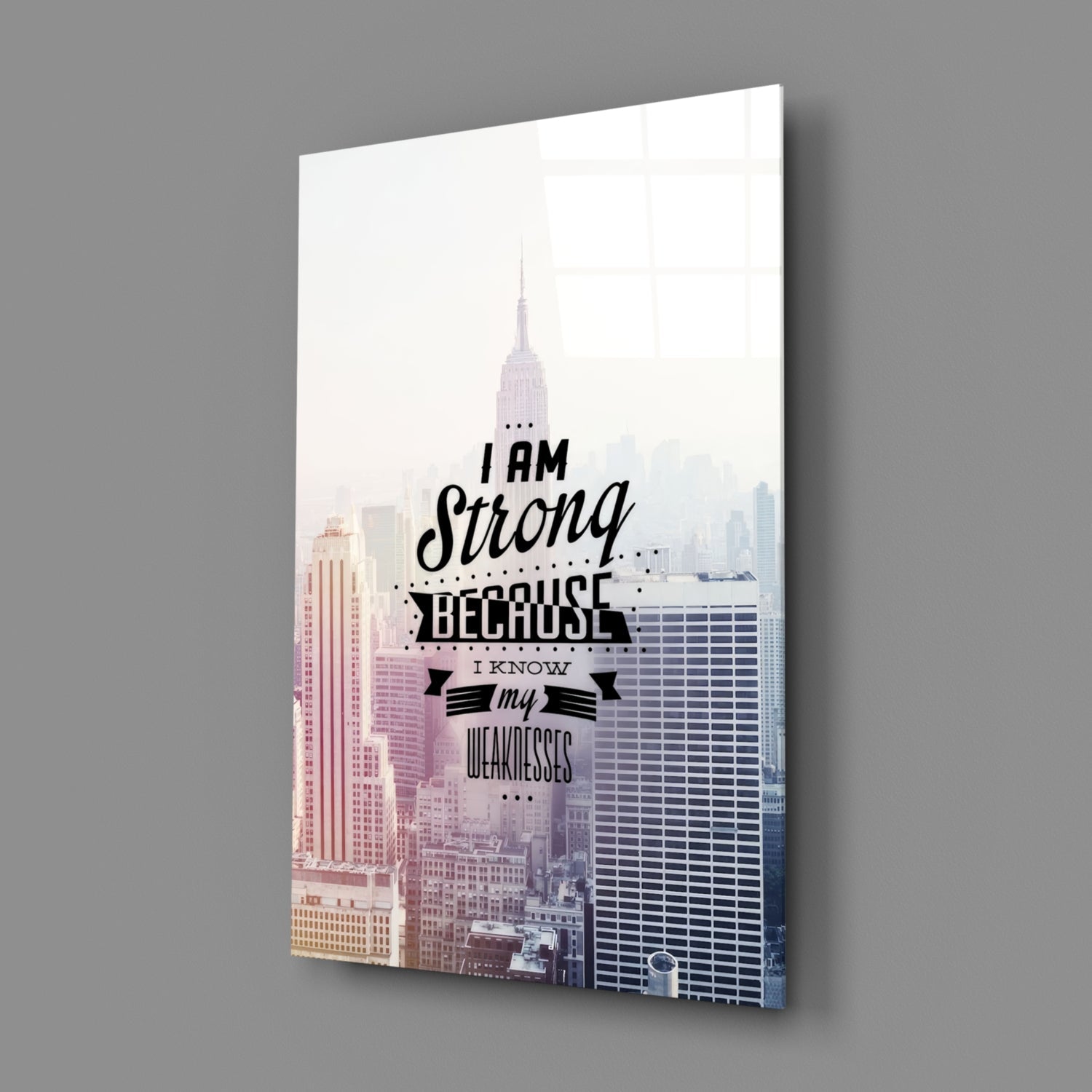 Glass wall art featuring New York City skyline with motivational text "I am Strong Because I Know my Weaknesses" in black lettering, displayed at an angle against gray background.