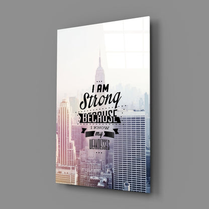 Glass wall art featuring New York City skyline with motivational text "I am Strong Because I Know my Weaknesses" in black lettering, displayed at an angle against gray background.