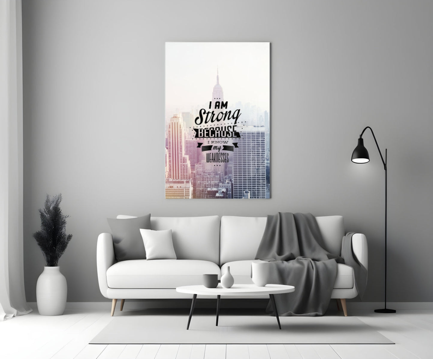 Motivational glass wall art featuring a cityscape with "I am Strong Because I Know my Weaknesses" text displayed above a modern white sofa.