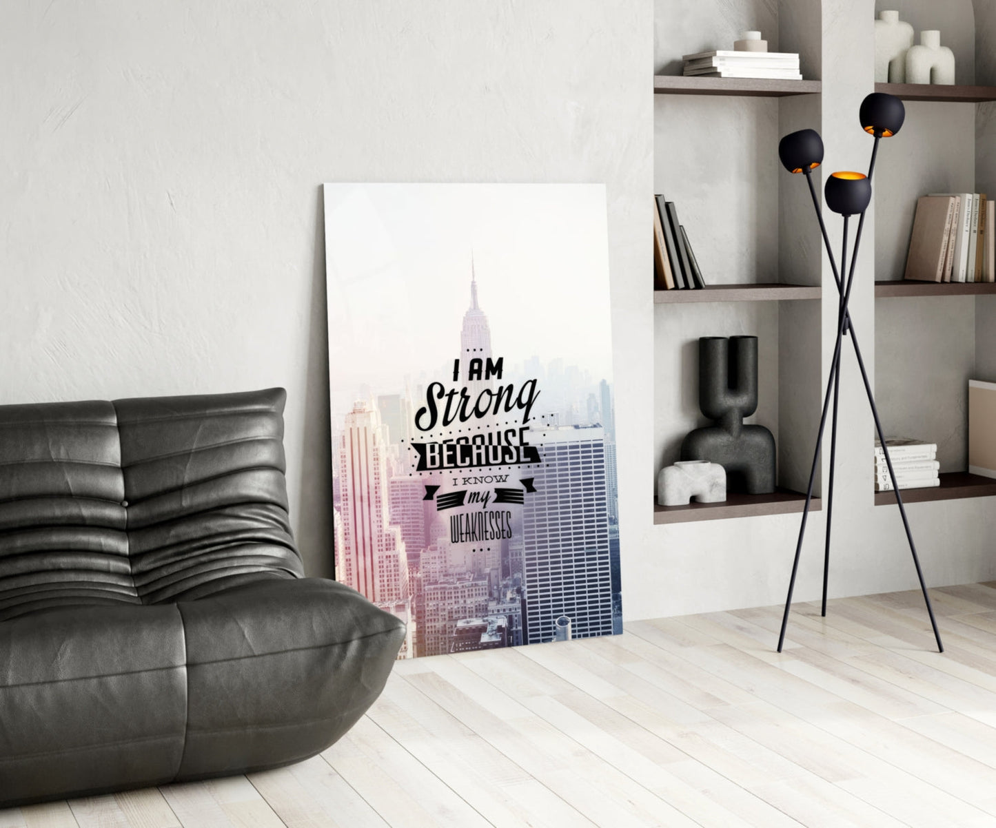 Glass wall art with New York City skyline and "I am Strong Because I know my Weaknesses" text, displayed in modern living room with black leather chair and shelving.