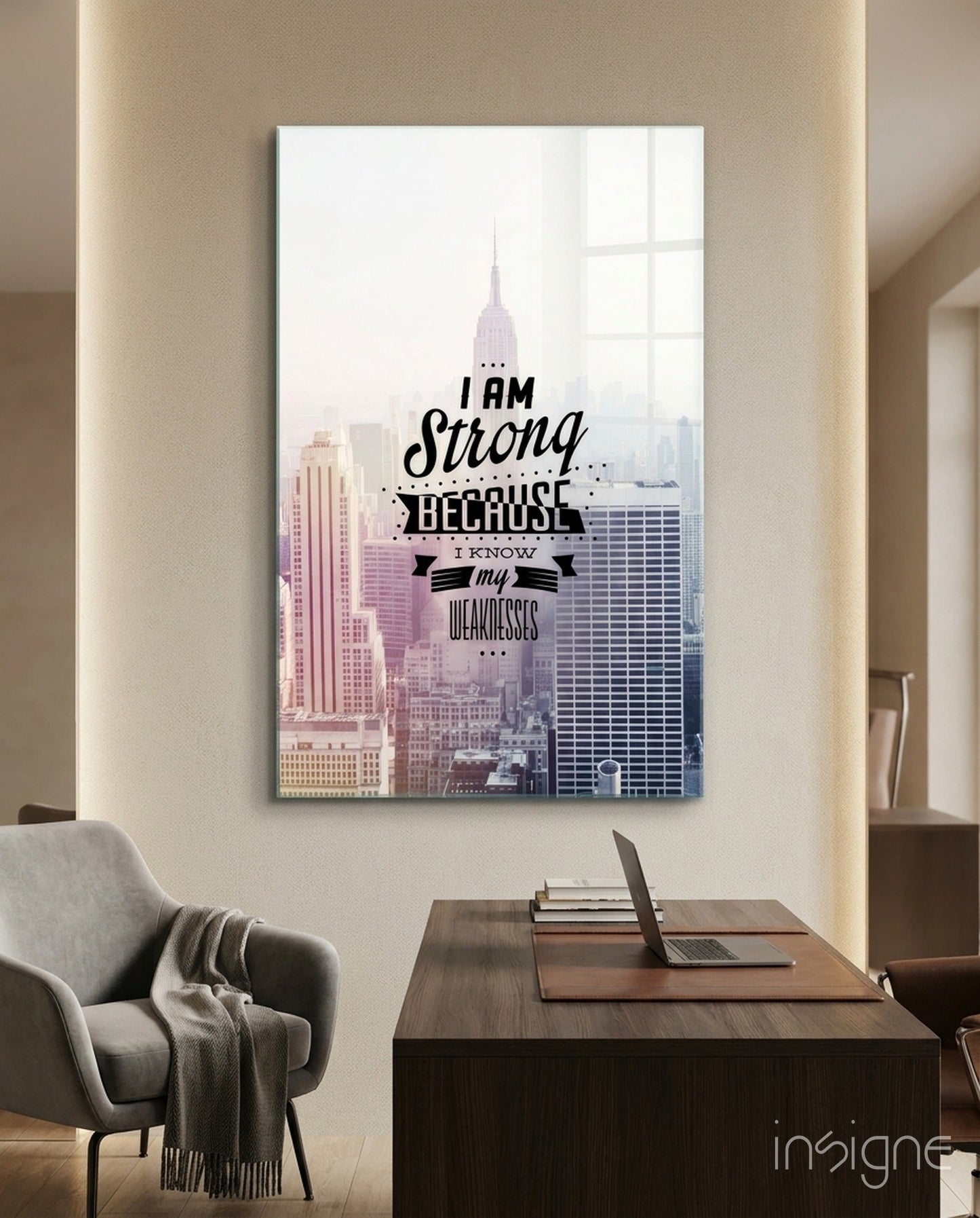 Glass wall art featuring New York City skyline with Chrysler Building and motivational text "I am Strong Because I Know my Weaknesses" displayed above desk in modern office setting.