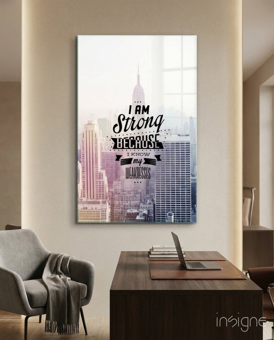Glass wall art featuring New York City skyline with Chrysler Building and motivational text "I am Strong Because I Know my Weaknesses" displayed above desk in modern office setting.