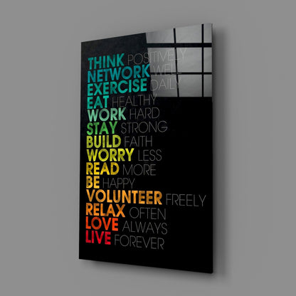 Angled perspective of black glass wall art with colorful gradient text listing life advice from "think" to "live forever," displayed against gray background.