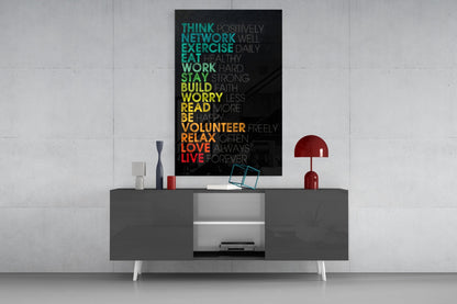 Motivational glass wall art with colorful gradient text mounted above a gray console table in a modern interior setting.