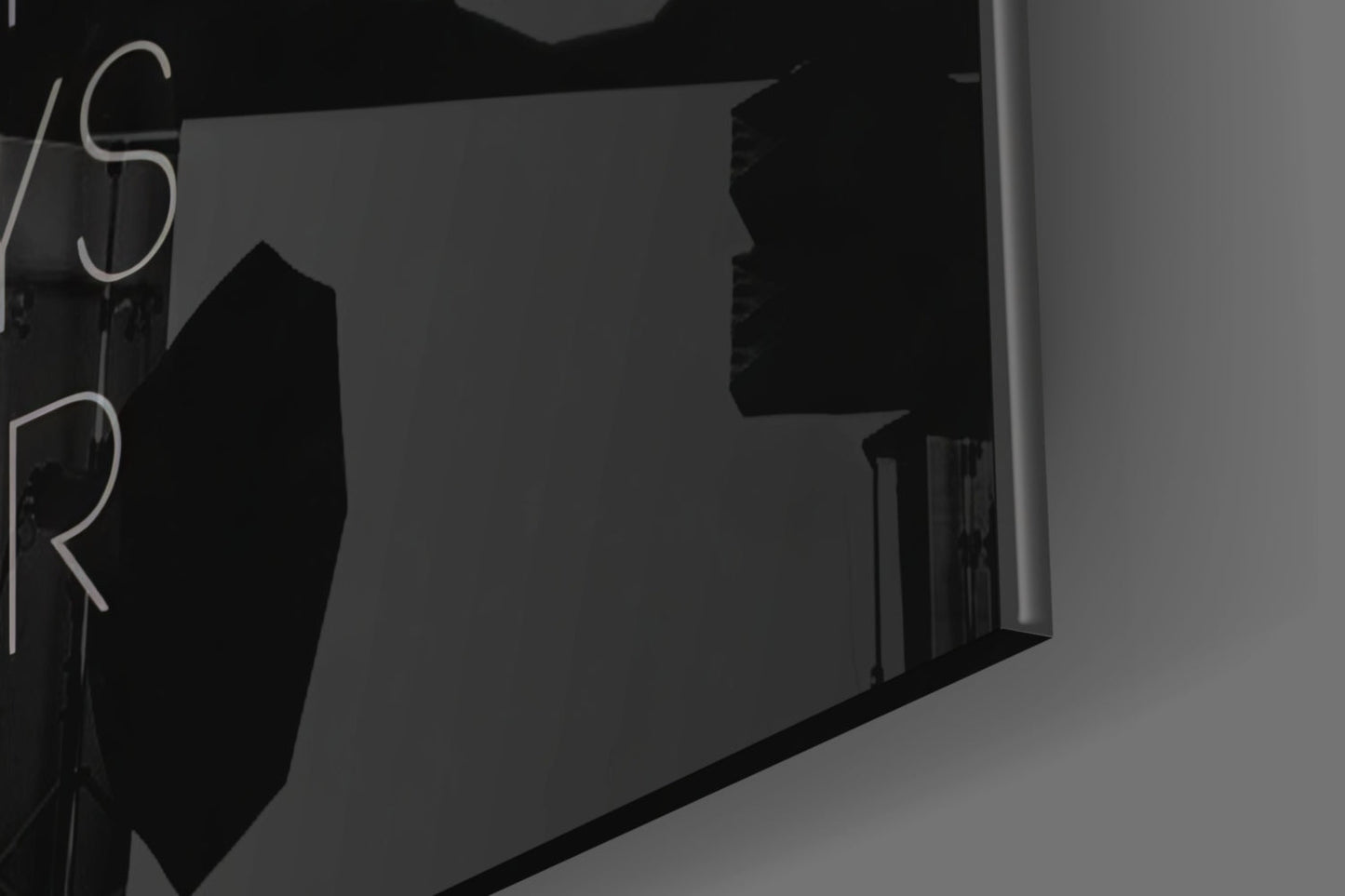 Black and white angled view of glass wall art displaying partial neon-style lettering on dark interior wall.