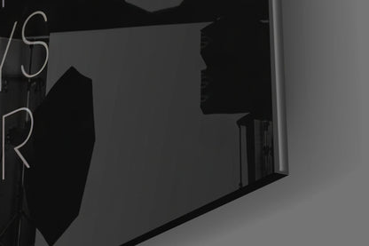 Black and white angled view of glass wall art displaying partial neon-style lettering on dark interior wall.
