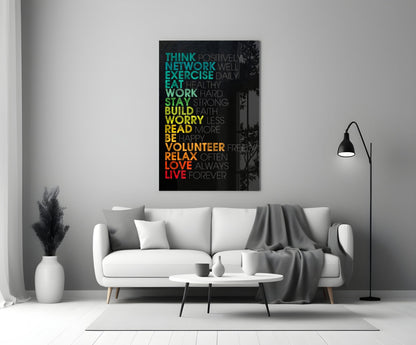 Colorful motivational glass wall art with gradient text from teal to red displayed above a white sofa in a modern living room.