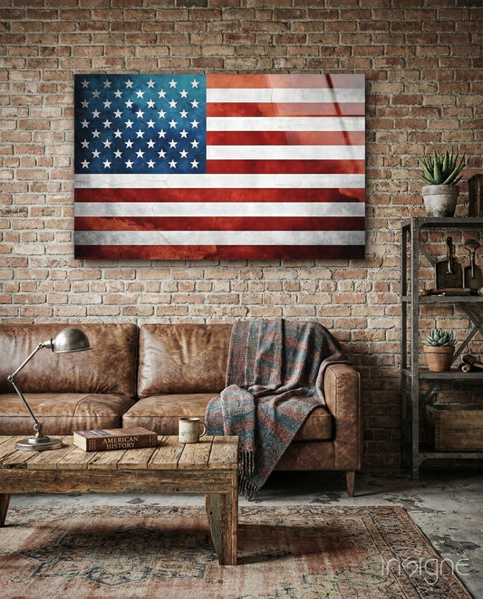 Vintage watercolor American flag glass wall art displayed above a brown leather sofa in an industrial loft setting with exposed brick.