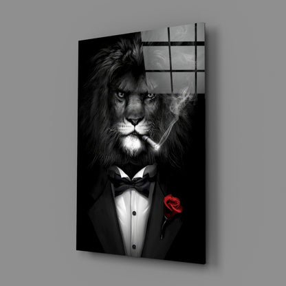 Black and white glass wall art depicting a lion in formal tuxedo with bow tie and red rose, shown at angled perspective against gray background.