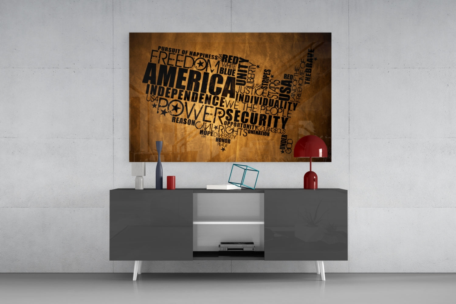 USA map word art glass wall panel in gold and black mounted above gray media console with red lamp and accessories.