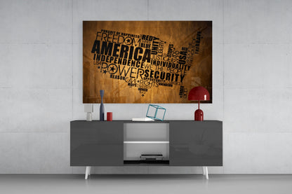 USA map word art glass wall panel in gold and black mounted above gray media console with red lamp and accessories.
