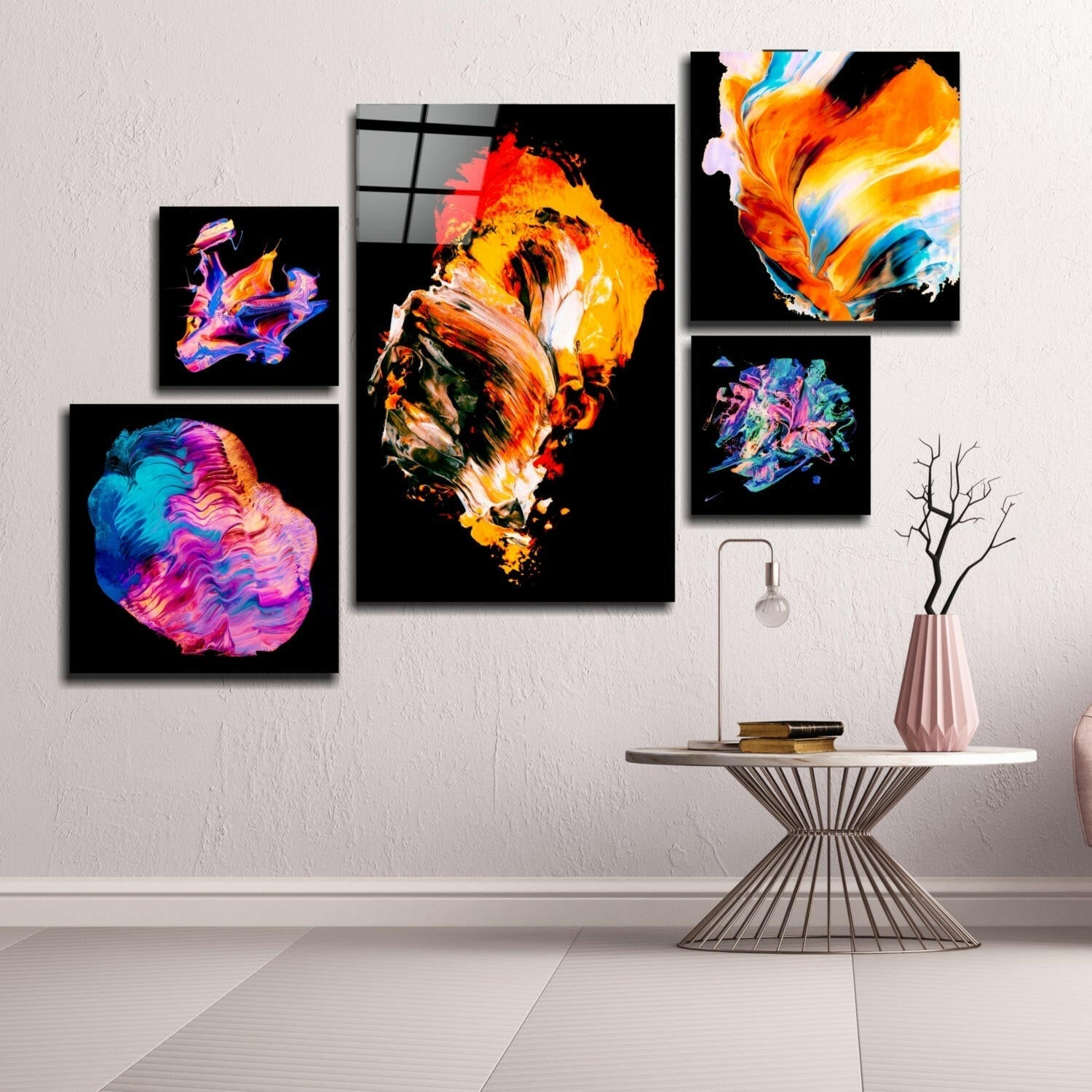 Modern interior scene displaying five vibrant abstract glass wall art pieces with neon orange, blue, and pink colors arranged asymmetrically above a geometric side table with decorative vase.