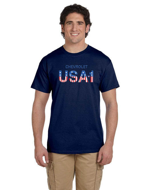 Front view of a smiling man with dark wavy hair in a navy t-shirt printed with CHEVROLET and striped USA-1 lettering, khaki cargo pants.
