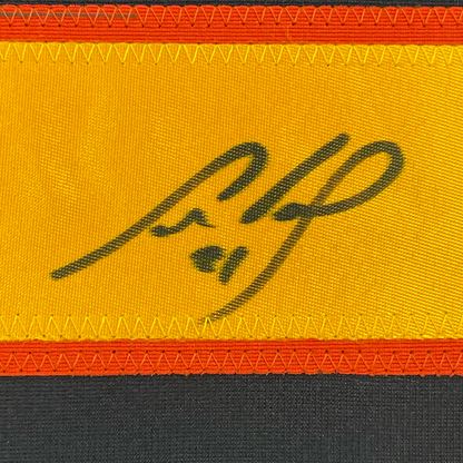 Close-up of signed autograph on yellow fabric strip with red and black borders, showing handwritten signature in dark ink.