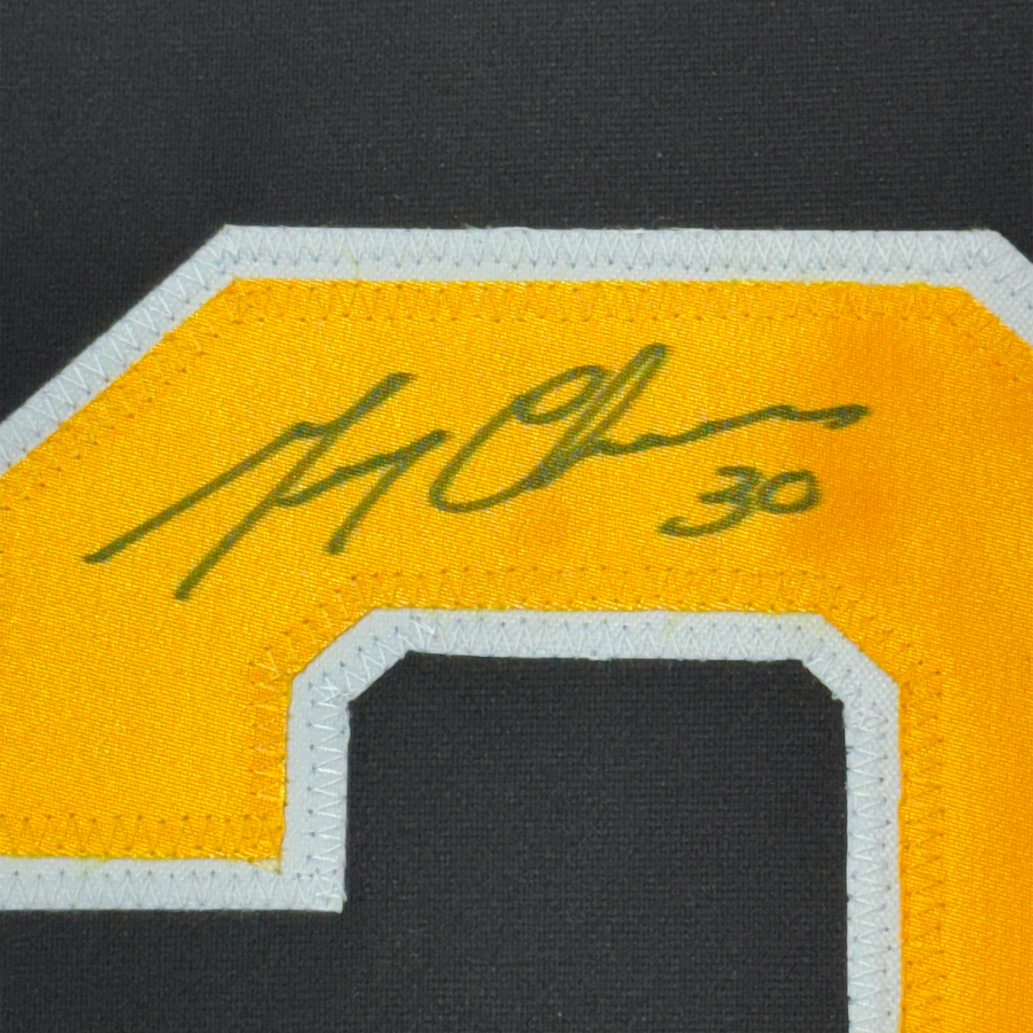 Close-up of green handwritten signature on yellow jersey fabric with white and black trim visible at bottom edge.