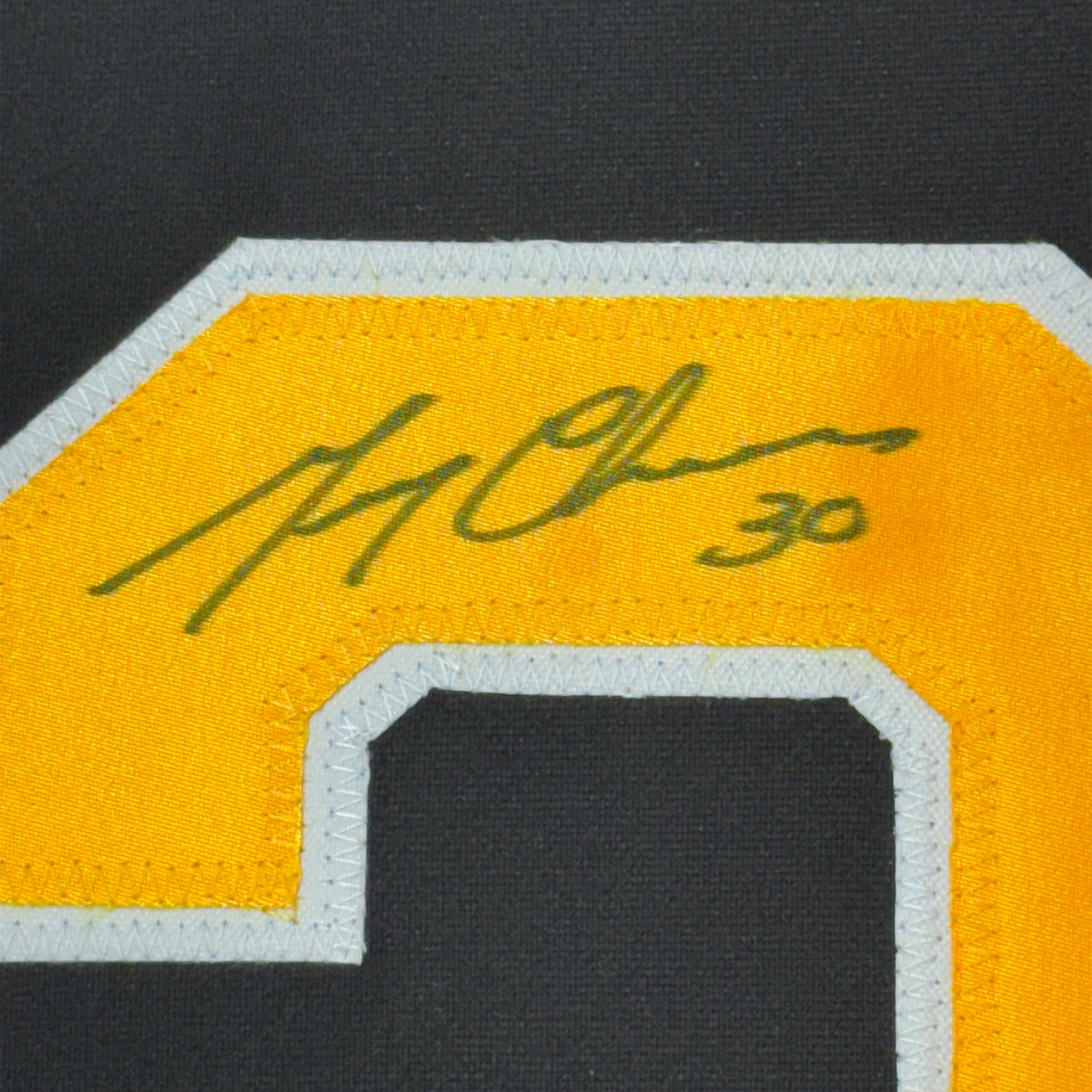 Close-up of green handwritten signature on yellow jersey fabric with white and black trim visible at bottom edge.