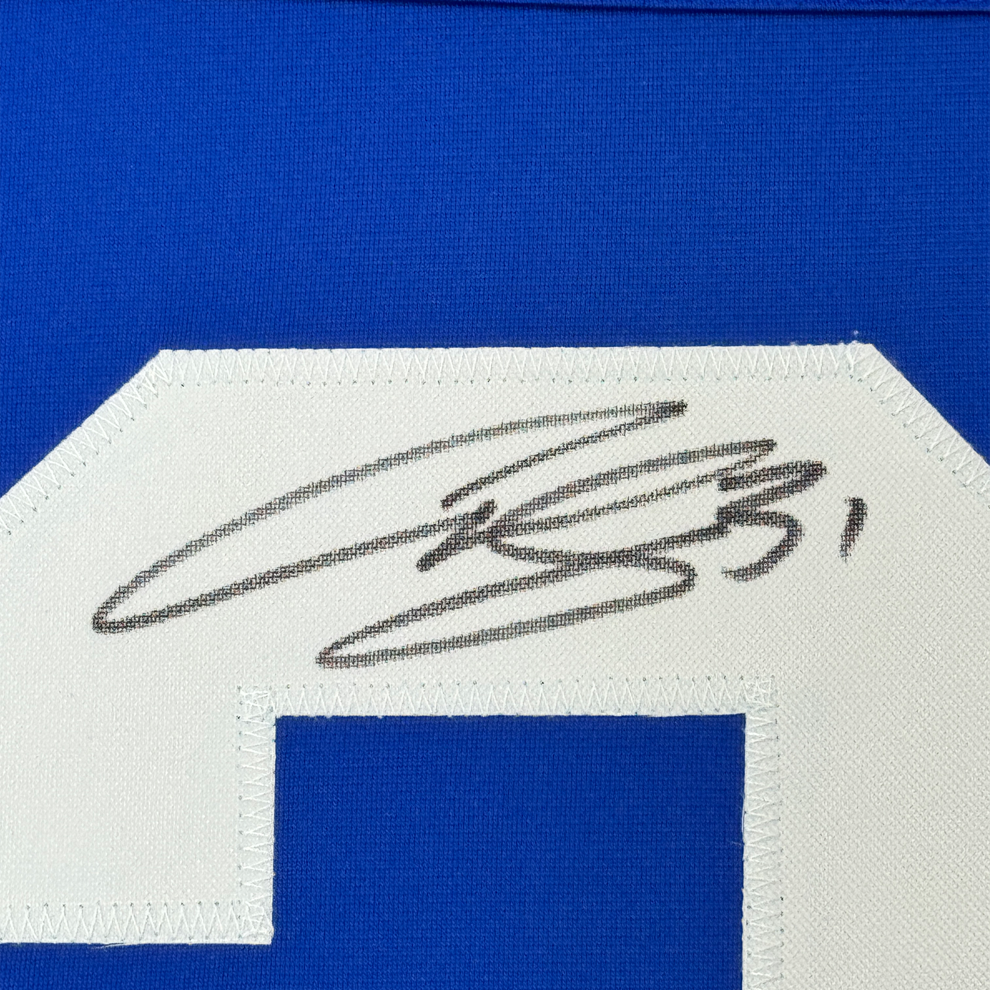 Close-up of autographed blue and white hockey jersey label showing black ink signature on white fabric strip against bright blue background.
