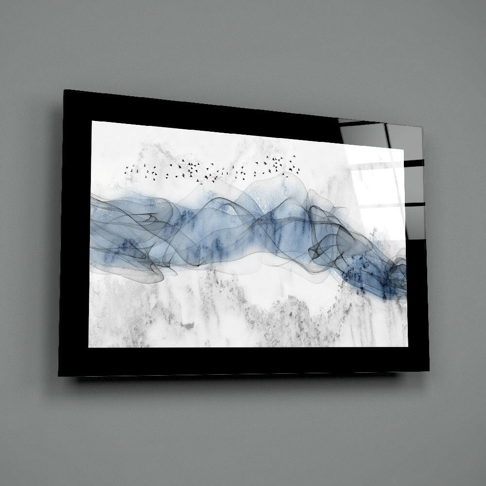 Black-framed glass wall art mounted on gray wall displaying blue watercolor waves with flying birds and textured gray landscape elements.