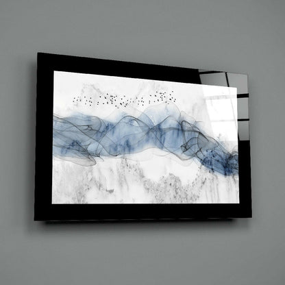 Black-framed glass wall art mounted on gray wall displaying blue watercolor waves with flying birds and textured gray landscape elements.