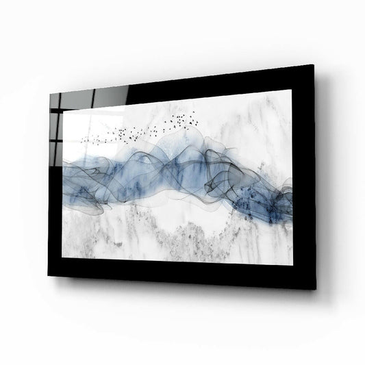 Blue Nebula Glass Wall Art displayed at an angle, showing abstract blue and gray watercolor-style waves with flying birds against white background in black frame.